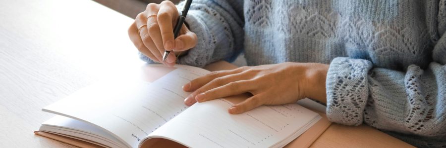 personne en pull bleu écrivant dans un agenda